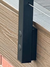 Close-up of a black side-mounted cable post fastened to a composite deck fascia.