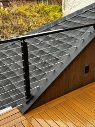 Black cable railing steps down along an angled roof wall on a composite deck.