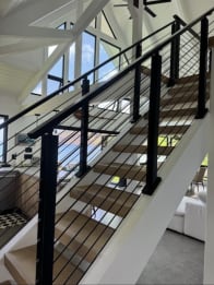 Black square posts and horizontal rods follow an open-riser oak stair on white stringers.