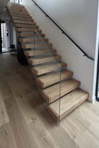 Connected oak Stack stair with frameless glass and a black wall handrail in a bright stairwell