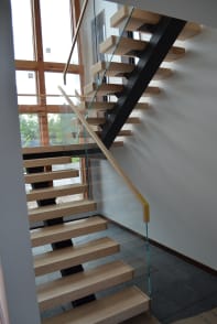 Maple floating treads on a black mono stringer with frameless glass and a maple handrail by tall windows