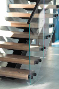 Close view of stained oak floating treads and black standoff pins holding a frameless glass guard.