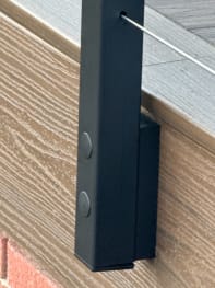 Close-up of a black side-mounted cable post fastened to a composite deck fascia.