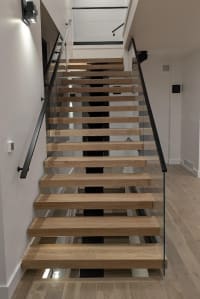 Thick white oak floating treads on a mono stringer with frameless glass and a black wall handrail.