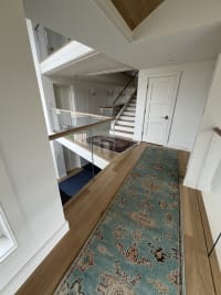 Frameless glass and wood top cap guard a stair opening beside a patterned runner