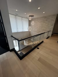 Black base rail glass wraps a stair opening above a white oak FLIGHT switchback in a stone-walled entry