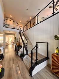 Black post glass railing runs up a stair and across the loft of a bright two-story entry