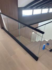 Black base rail glass with a black cap edges a stair opening beside a walnut-paneled wall