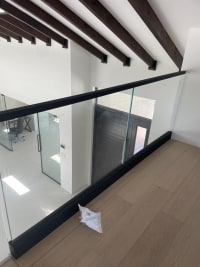 Black base rail glass with slim cap below dark ceiling beams overlooking a bright foyer