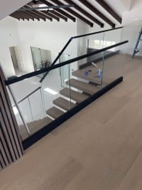 Black base rail glass and cap curve around a floating oak stair beside wood slat panels