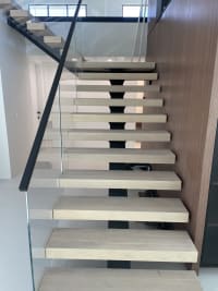 Long straight run of white oak floating treads on a black mono stringer with frameless glass and black handrail