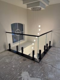 Frameless glass on black talon spigots with a black cap wraps a loft beside a cascading crystal pendant and arched window