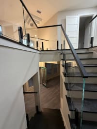 Frameless glass on black talon spigots runs up a dark-tread stair to a vaulted loft