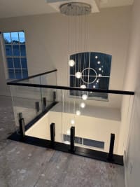 Frameless glass on black talons with a black cap overlooks a two-story foyer with a glowing orb pendant