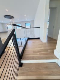 Black cable stair railing transitions to frameless glass in a base rail along a white oak upper landing.