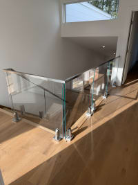 Frameless glass panels on stainless spigots with a stainless cap rail surround a stair opening on oak flooring.