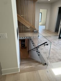 Glass panels on black standoff pins with a black handrail guard a stair opening beside a slatted wood wall.