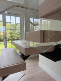 Close detail of thick white-oak floating treads and frameless glass panels against windows.