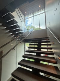 Dark wood FLIGHT Mono treads with Vedera glass and stainless handrails rise toward a two-story window.