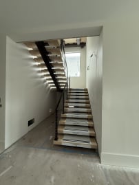Black mono stringer switchback stair with white oak treads and black cable railing in a narrow stairwell