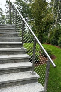 Brushed stainless posts with a 2-inch round handrail and cable infill climbing a long granite garden stair.