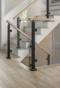 Black posts hold glass panels capped by a light wood handrail along a white-riser staircase.