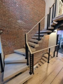Switchback floating stair with pale oak treads and black cable railing along an exposed brick wall
