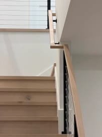 Oak stair treads with black cable railing and a white oak handrail turning at a landing
