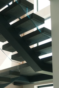 Underside view of dark gray wood floating treads on a black stringer with a glass railing edge.