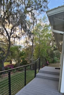 Black side-mounted cable railing lines a gray composite walkway and steps past azaleas.