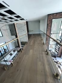 Frameless glass on brass talon spigots lines an oak-floored bridge over a living room