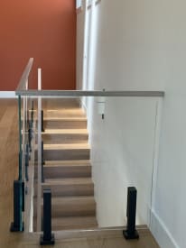 Black talon-mounted glass railing with wood cap rail guards the top of an oak staircase.