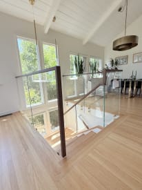 Frameless glass railing with a dark walnut handrail and posts guards a stair opening in a bright vaulted room.