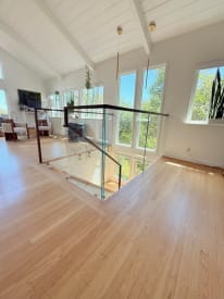 A glass railing with a walnut handrail surrounds a stair opening in a sunlit vaulted living space.
