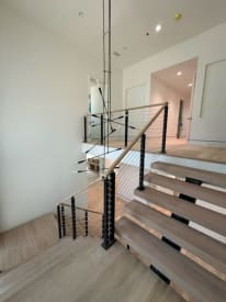 Black cable railing posts with a white oak handrail turn at the landing of a white oak floating stair.