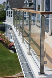 A run of stainless posts with glass clamps and hardwood cap lines a white balcony above hydrangeas.