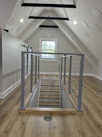 Silver cable railing guards a stair opening in a bright attic bonus room with wood floors.