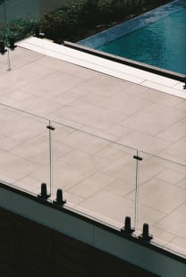 Frameless glass panels on black talon spigots edging a stone pool terrace.