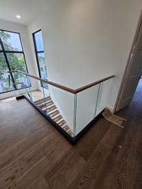 Black base rail glass with a wood top cap wraps a stair opening by tall arched windows