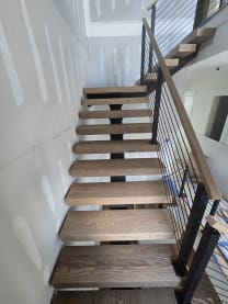 Thick red oak floating treads climbing beside black rod railing and an oak handrail