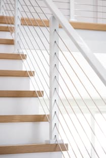 Close view of a white post with cable infill beside natural oak treads on white risers.