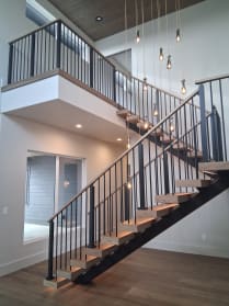 Black mono stringer stair with wood treads and black baluster railing rises past a window to an upper balcony.