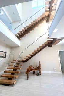 Looking up a wood mono-stringer floating stair with glass railing and a glass-railed loft above.