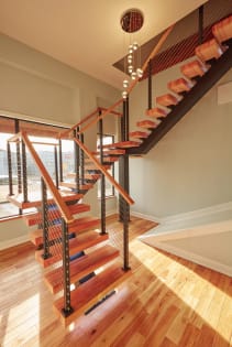 Warm wood floating treads on a black stringer with cable railing and wood handrail in a sunlit stairwell.