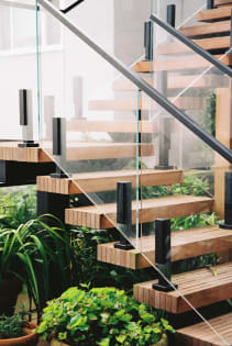 Slatted wood treads and black-post glass railing on an exterior FLIGHT stair surrounded by lush tropical plants.