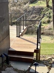 Black cable railing wraps an ipe deck and steps above a stone path