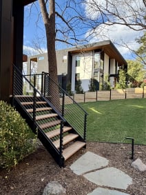 Black steel exterior stair with ipe treads and cable railing beside a modern home