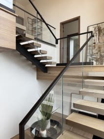 White oak floating switchback with frameless glass and black handrail around a stair opening with modern art