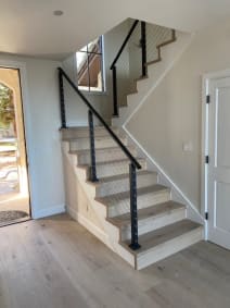 Black-post cable railing and handrail climb a white oak stair beside an arched door