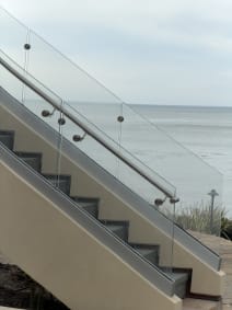 Frameless glass on stainless standoff pins with a stainless handrail lines an exterior stair overlooking the ocean.